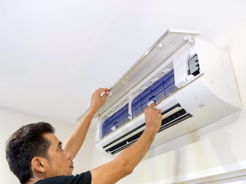 A man is removing the air filter of the air conditioner for cleaning.